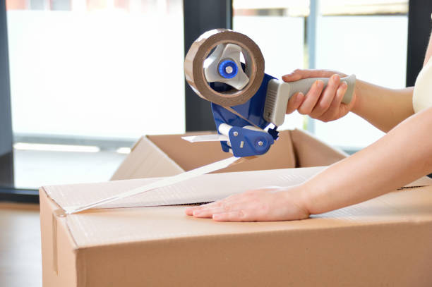 Shot of an unidentifiable young woman closing a cardboard box with tape at home